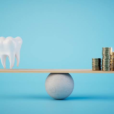 A scale on which a model tooth and stacks of coins are balanced
