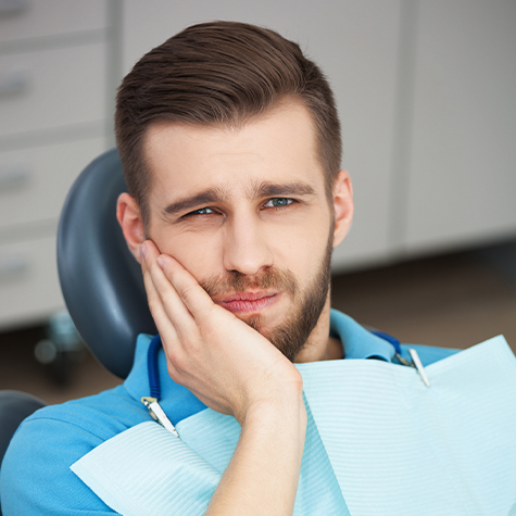 Man in need of emergency dentistry holding cheek in pain