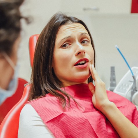 Woman talking to her dentist and holding her cheek