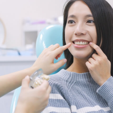 Woman pointing to flawless smile after dental implant tooth replacement