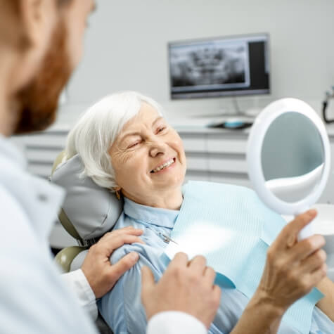 Woman looking at smile after dental implant tooth replacement