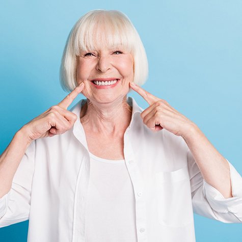 a woman pointing at her smile with dentures
