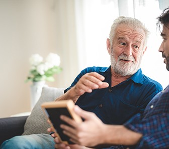 Two men in blue shirts on couch talking over picture frame