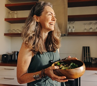 Woman in kitchen smiling carrying wooden salad bowl