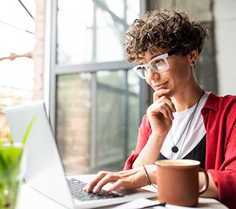 Person with curly hair in red sweater working on laptop