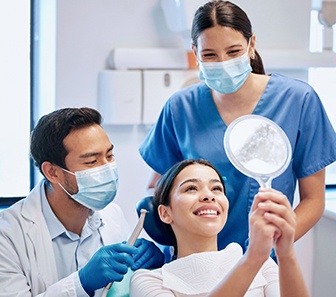 Dentist, dental assistant, and patient smiling at reflection in mirror