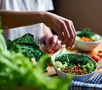 Closeup of someone’s hand with orange nails placing veggies in bowl for salad