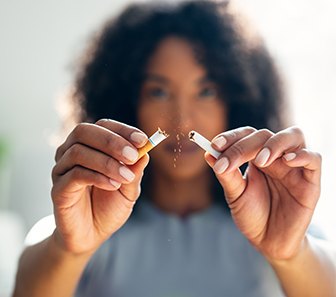Woman in gray shirt breaking cigarette in half