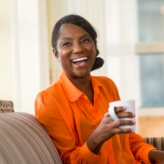 Smiling older woman in orange blouse holding white coffee mug