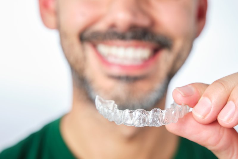 a man smiling and holding a clear aligner tray